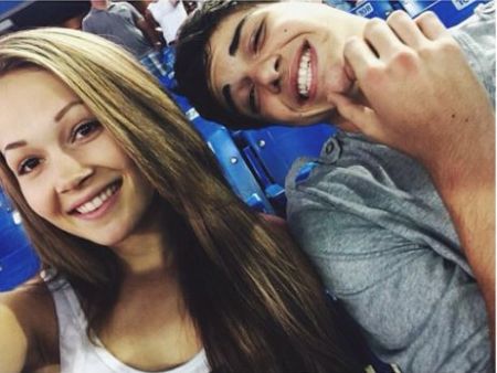 Noah Centineo in a grey t-shirt poses with former girlfriend Kelli Berglund at a baseball game.